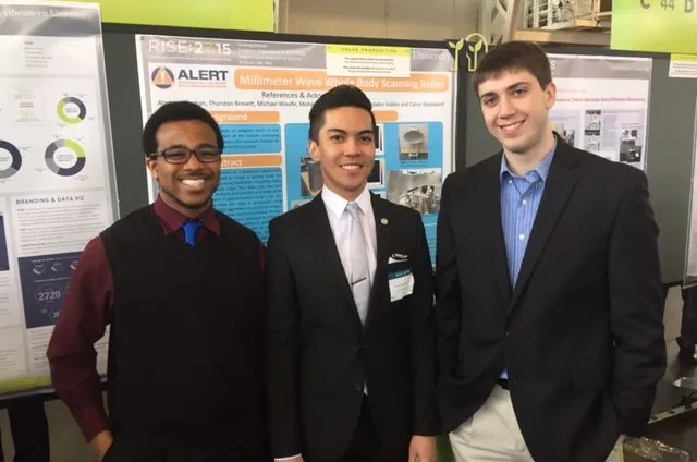 three students pose in front of a poster